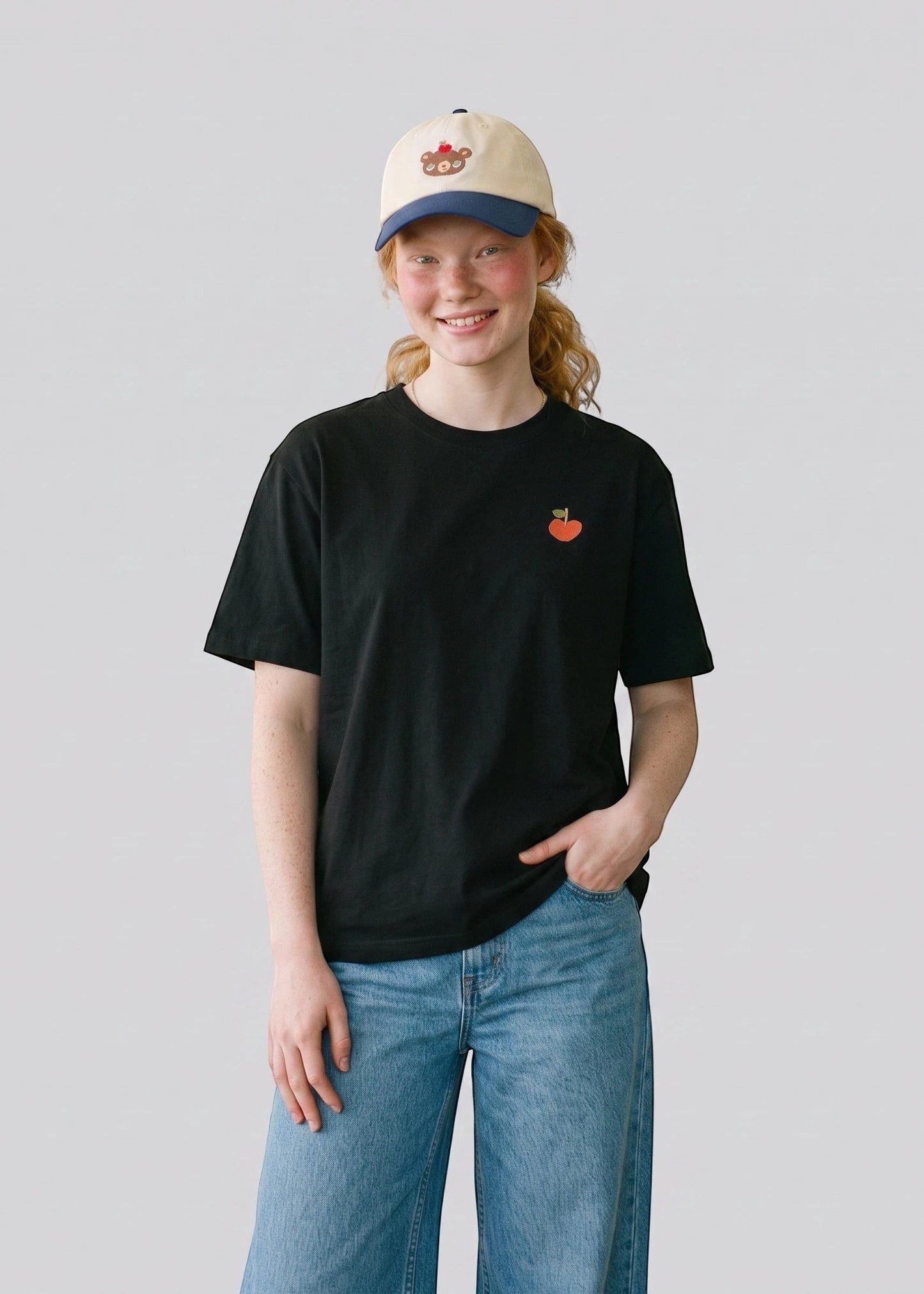 Via Artists oversized black cotton t-shirt with small apple embroidery worn by a model in jeans and a baseball cap