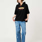 Via Artists black short-sleeve hoodie featuring a Nagasugiru Inu hot dog graphic, worn by a model with blue jeans.