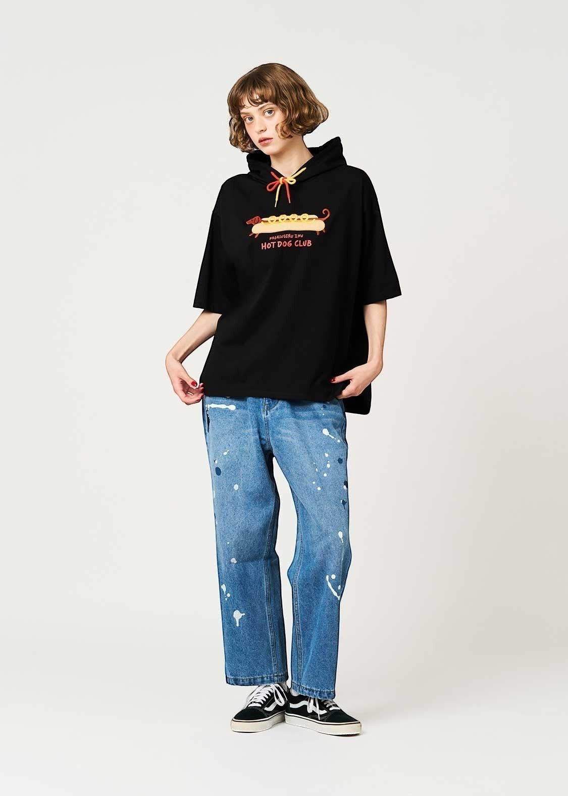 Via Artists black short-sleeve hoodie featuring a Nagasugiru Inu hot dog graphic, worn by a model with blue jeans.