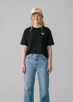Via Artists Helcovell Guard black oversized cotton t-shirt with small dragonfly graphic worn by a smiling woman
