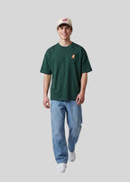 Via Artists Helcovell Rush oversized dark green cotton t-shirt worn by a smiling man with a beige cap and blue jeans