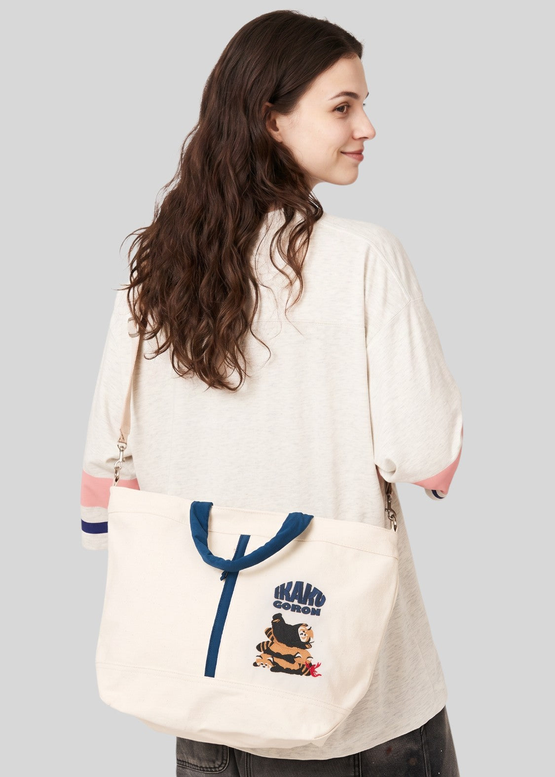 Via Artists Ikaku Goron 2-way cotton canvas tote bag with adjustable strap and embroidered graphic, worn over shoulder.