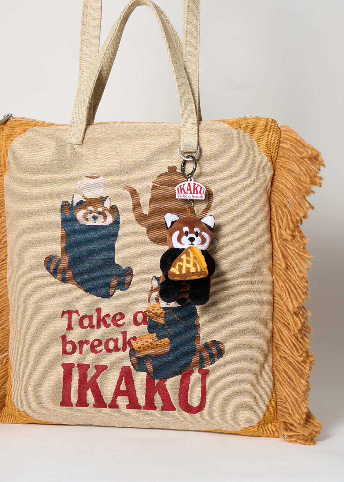 Via Artists Ikaku Take A Break jacquard tote bag in beige with red panda graphic, fringe sides, and plush charm.